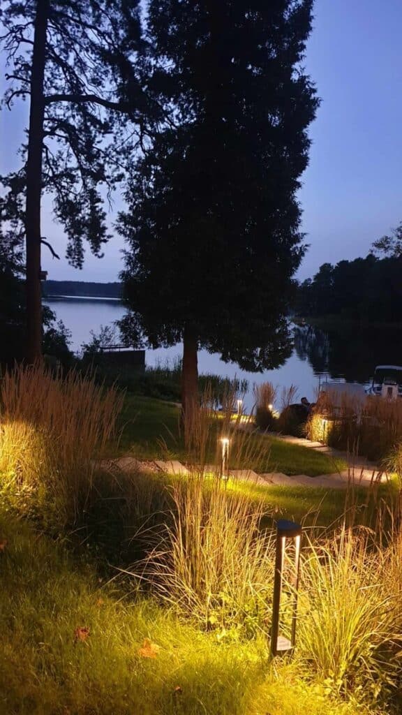 Domki nad jeziorem z ogrodem oświetlonym w blasku lamp wśród zieleni.