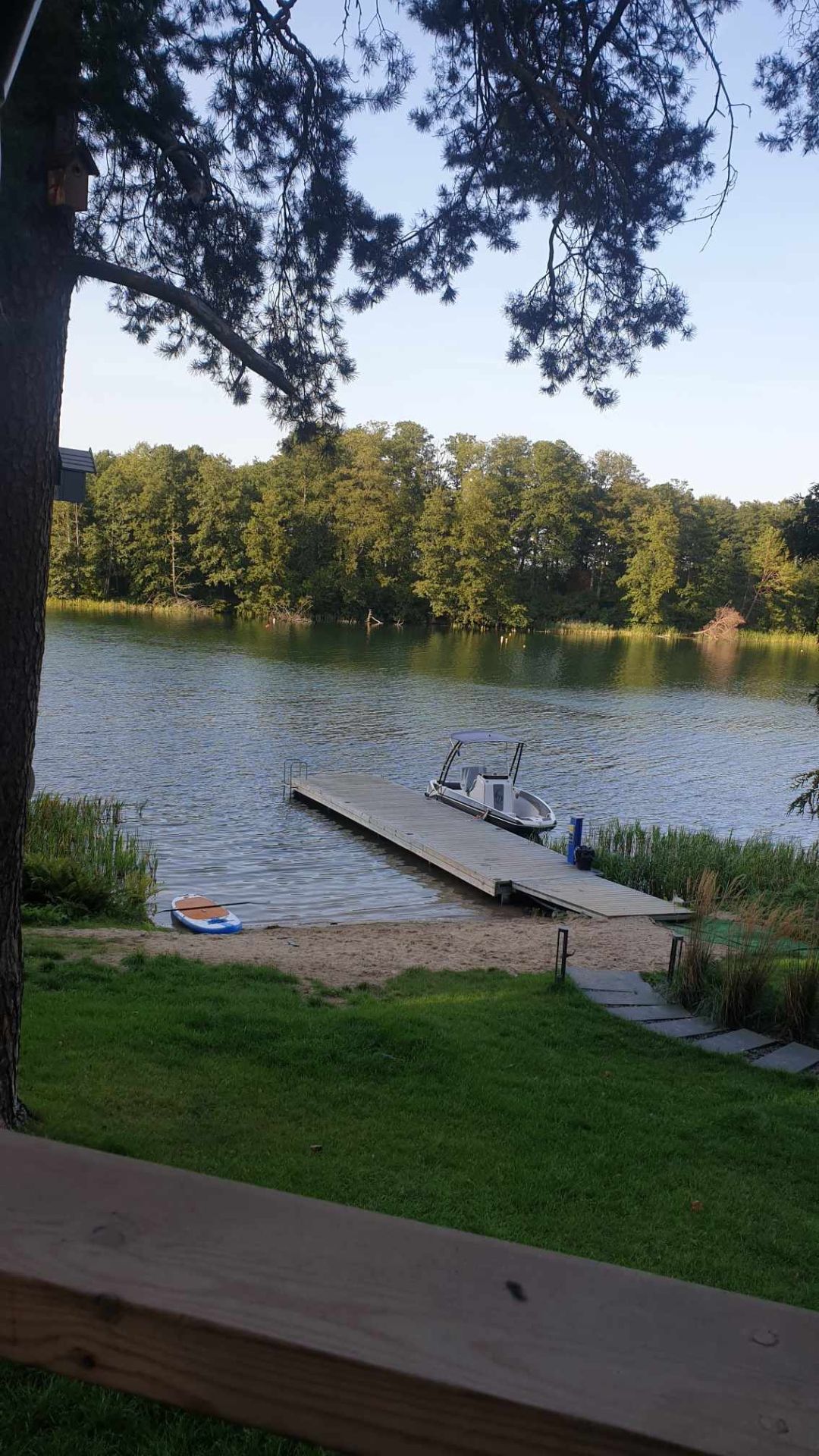 Domki nad jeziorem z widokiem na wodę, obok pomostu i łódki przy brzegu.
