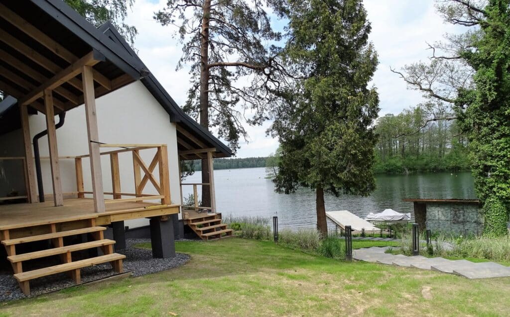 Domki nad jeziorem z możliwością wędkowania, otoczone zielenią i widokiem na wodę.